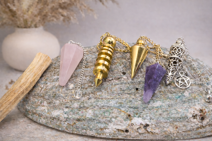 Différents pendules en laiton, améthyste, quartz rose et lapis-lazuli sur fond marbre | O'NAIA