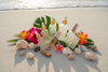 Huiles essentielles et roll-on aromachologie posés sur le sable blanc avec coquillages et vagues en été — bien-être olfactif O'NAIA