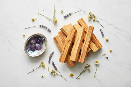 Flat lay de bâtons de Palo Santo, coquille d'ormeau, améthyste et fleurs séchées sur marbre blanc — rituel de purification O'NAIA